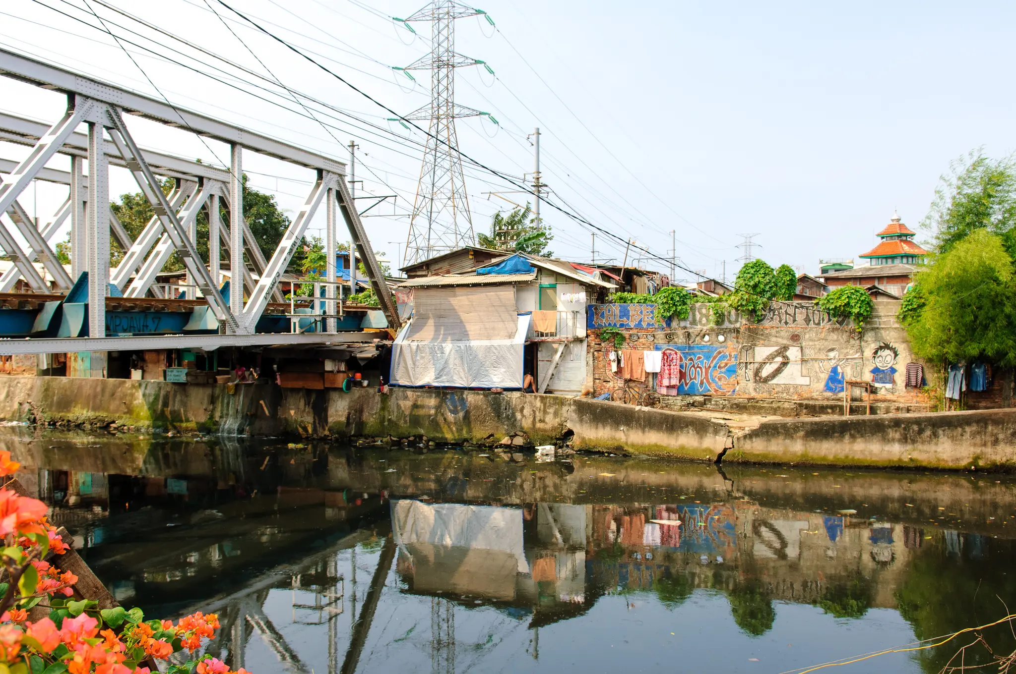 Vue large des mêmes habitations entre un pont métallique et un canal à Jakarta