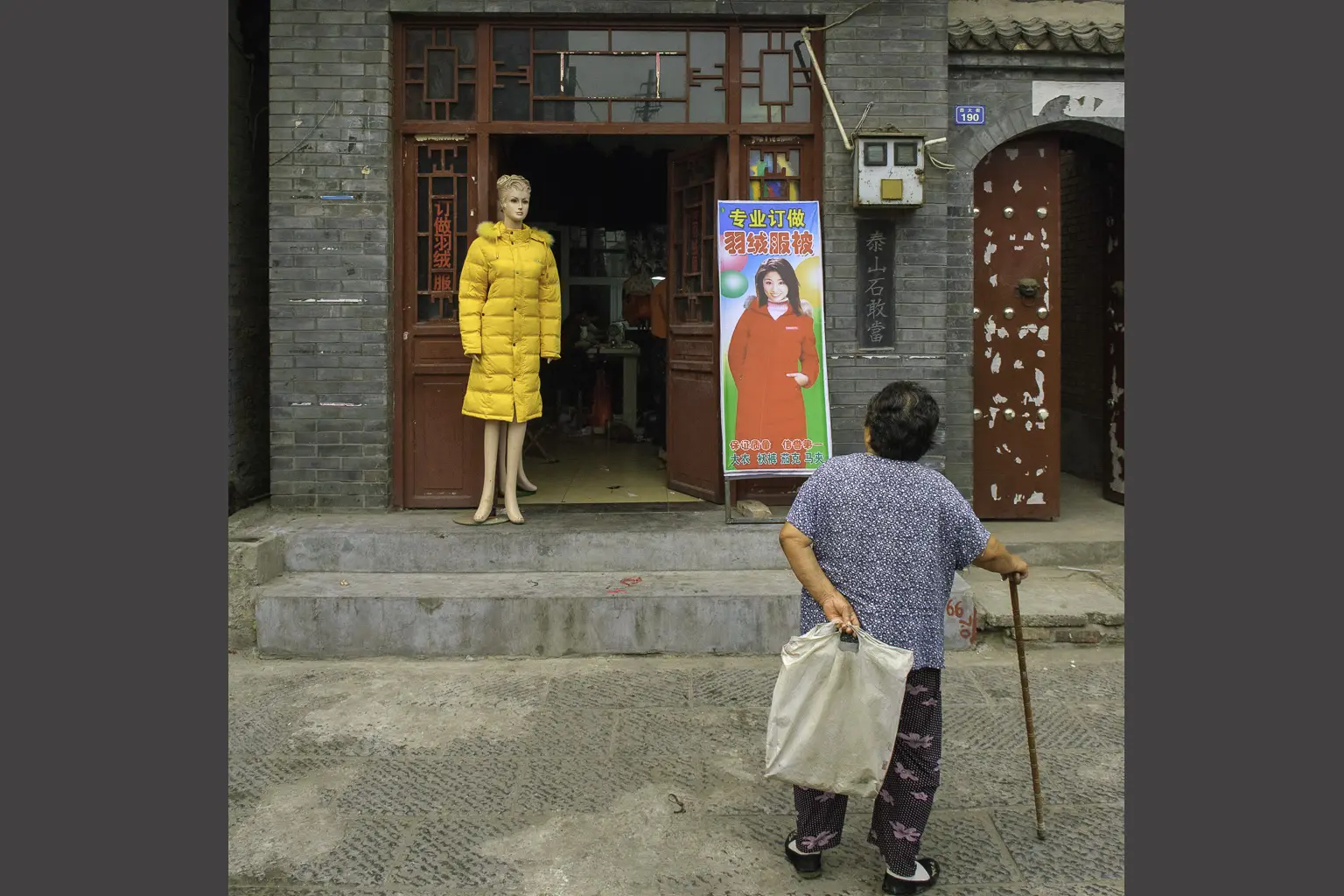 Une femme munie d’une canne regarde un mannequin vêtu d’une longue doudoune jaune devant une boutique chinoise