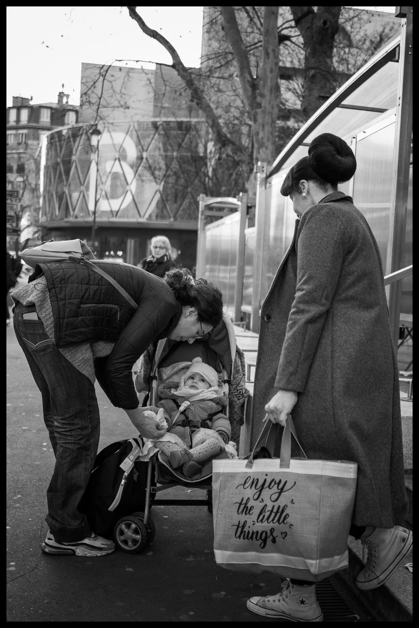 Une femme tient un sac portant l'inscription Enjoy the little things tandis qu'un bébé est installé dans une poussette juste à côté