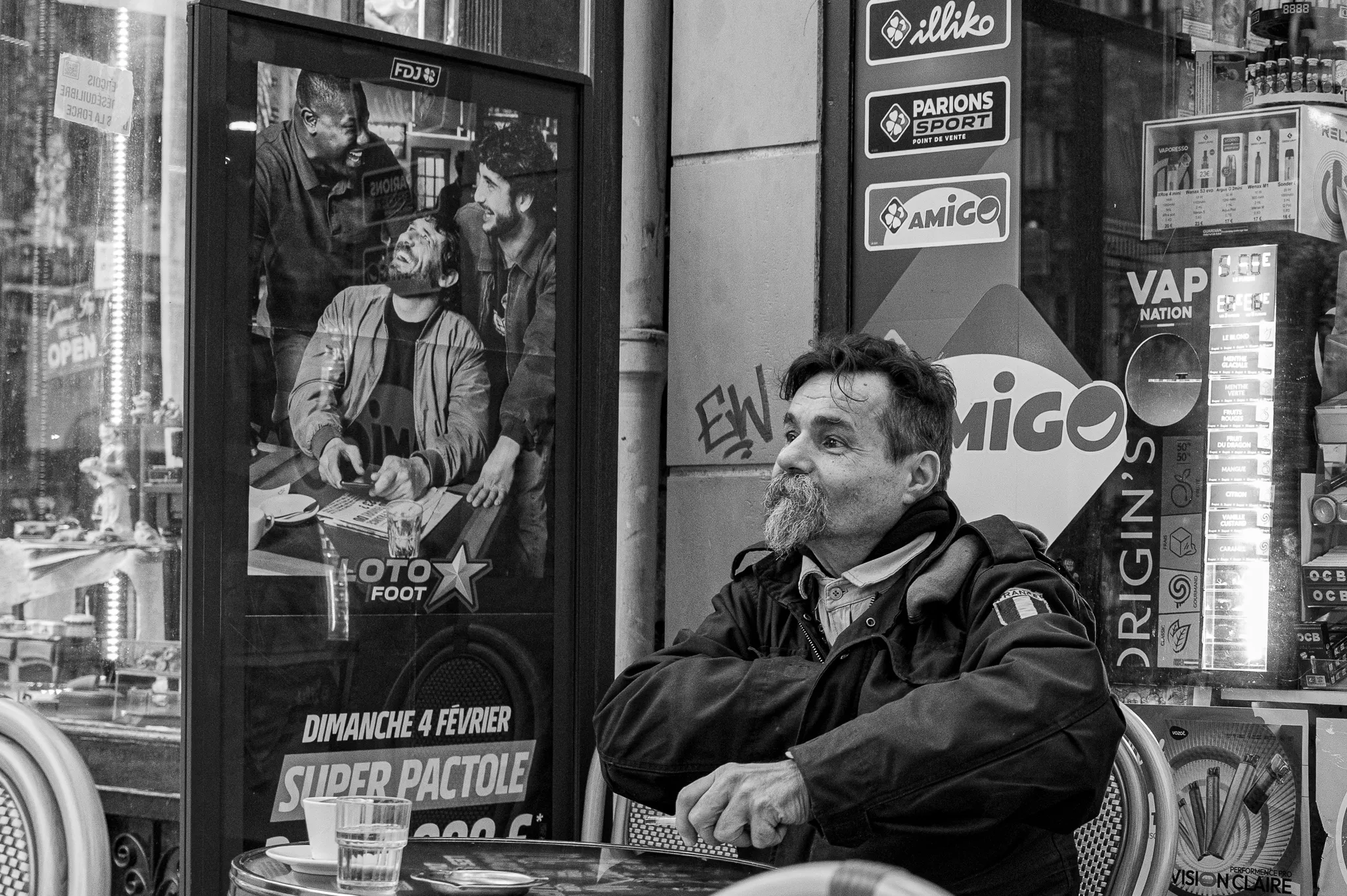 Un homme assis à un terrase de café parisien hésite à acheter un ticket de Loto