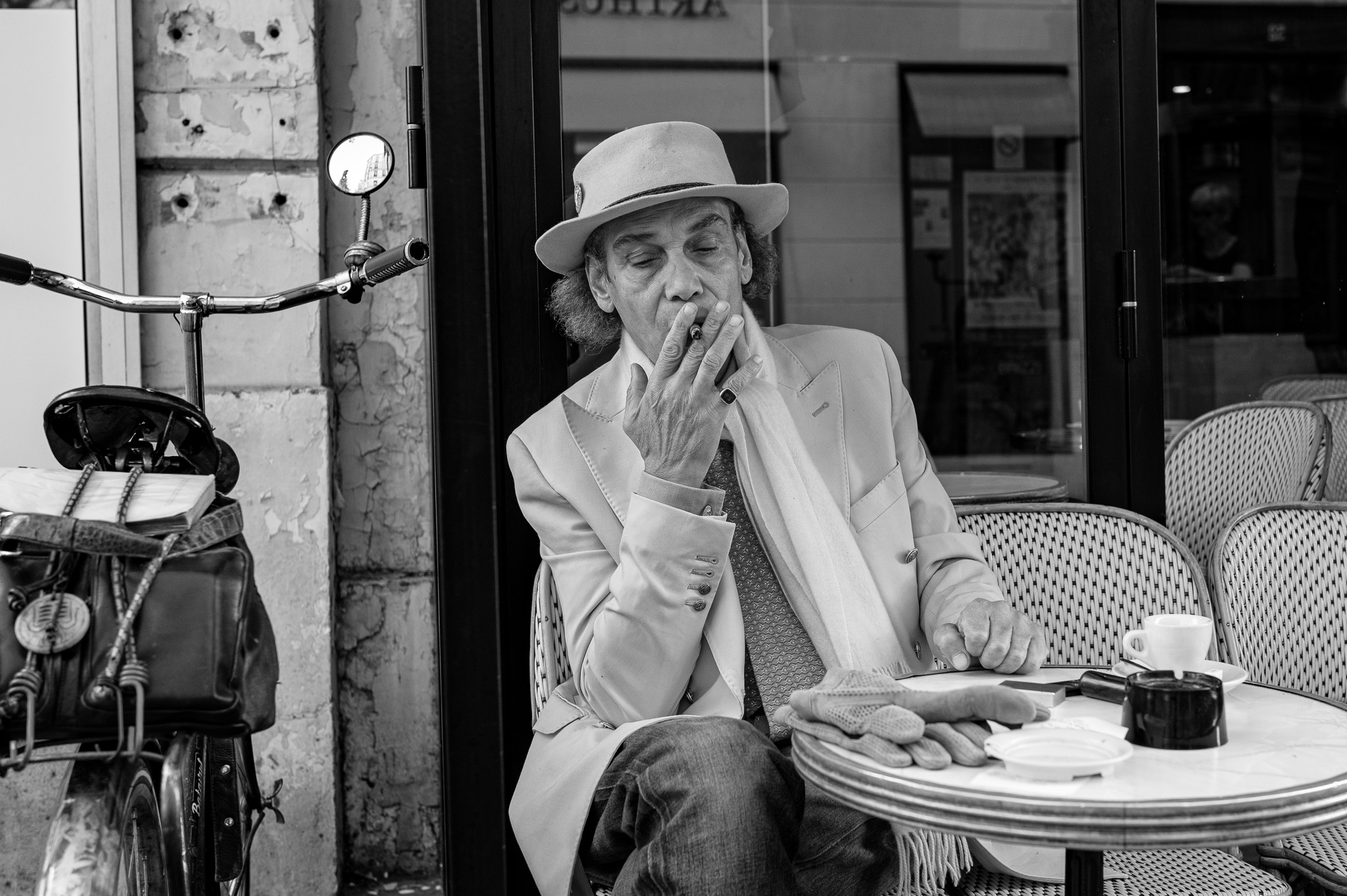 Une homme distingué fume un cigarillo à la terrasse 'un café parisien'