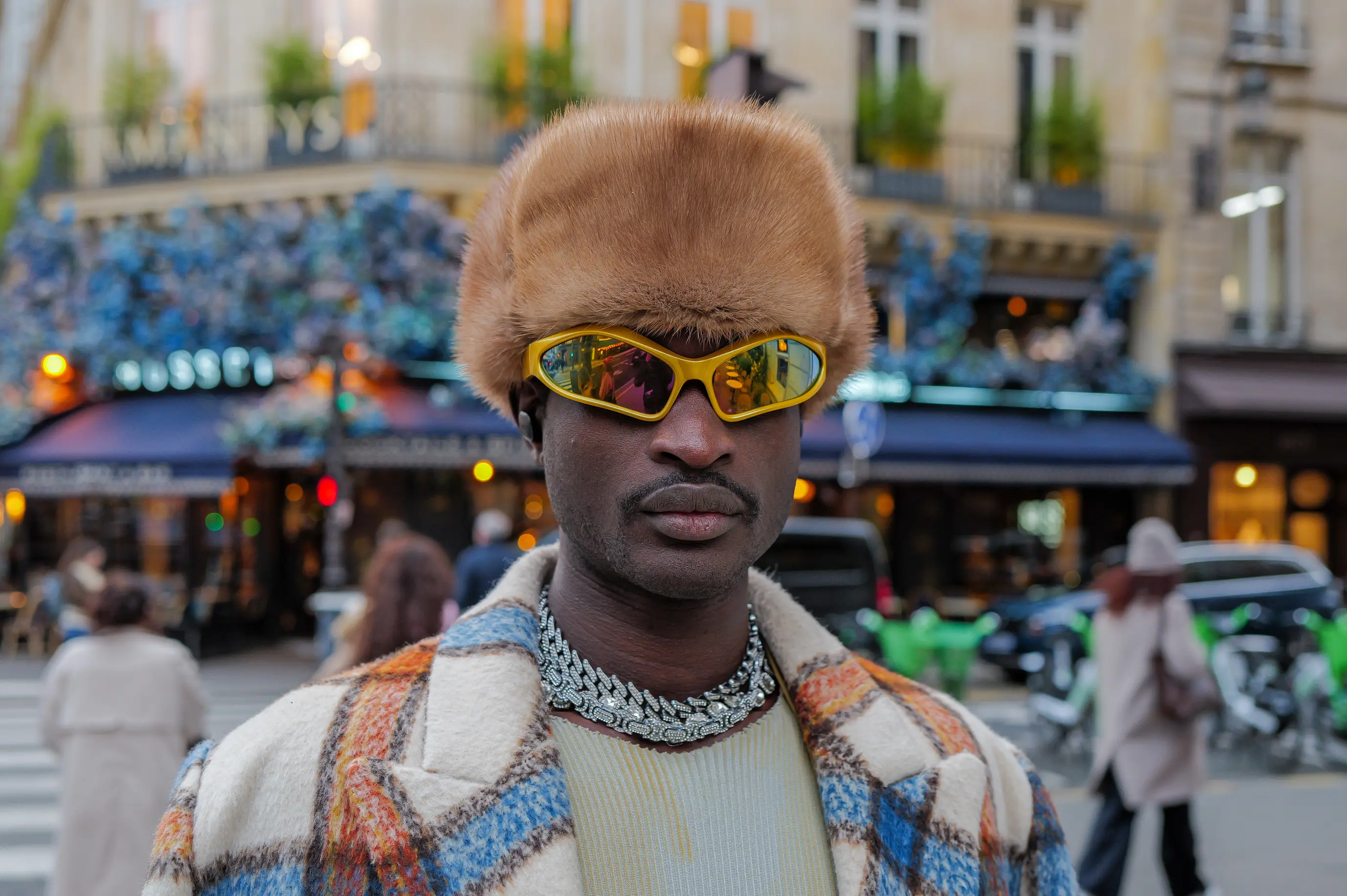 Portrait frontal d'un homme portant un grand bonnet de fourrure, des lunettes jaunes à verres miroir et un manteau à carreaux