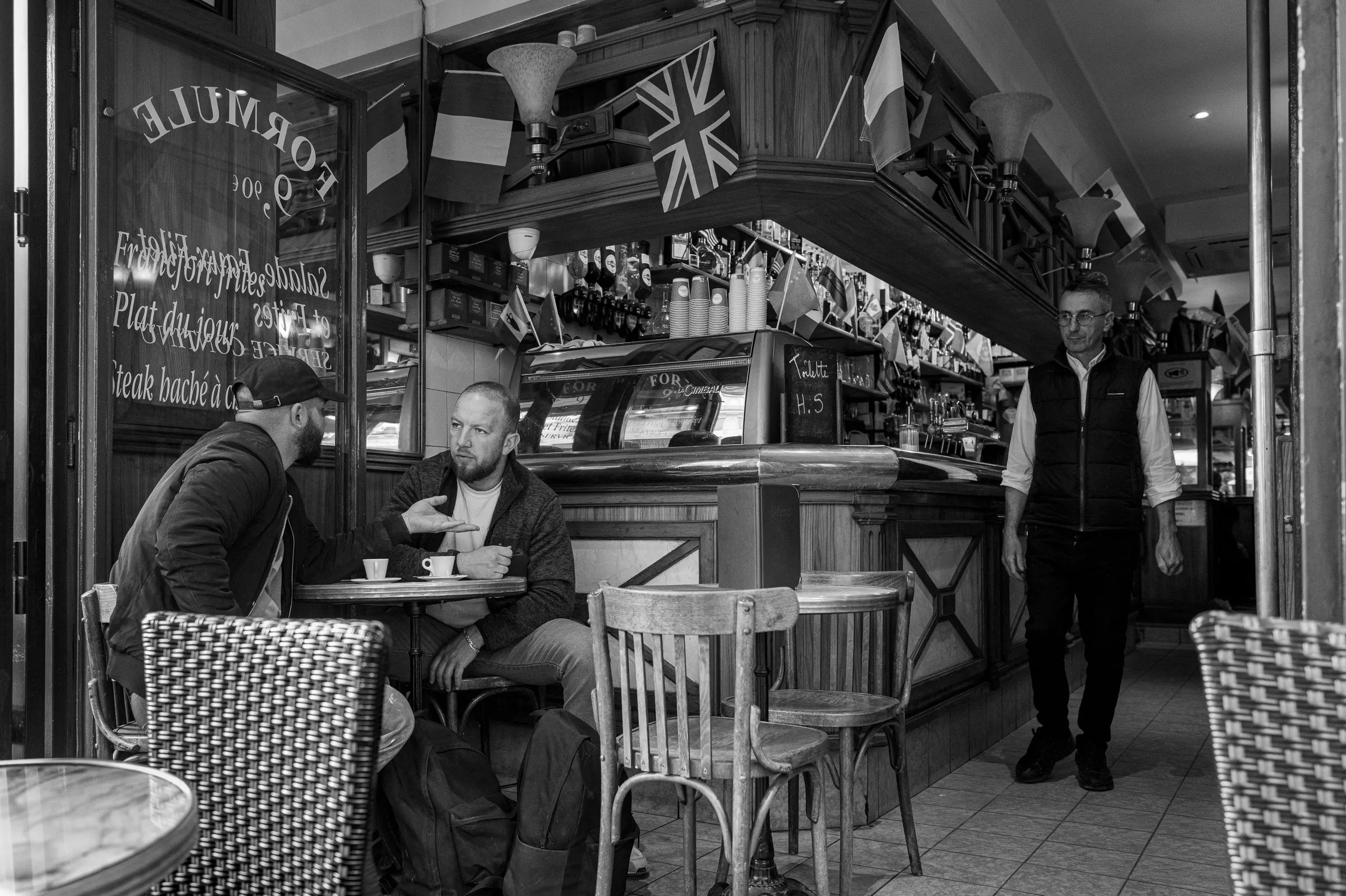 Au premier regard, deux hommes discutent à une table. L’un parle avec la main, l’autre l’écoute.