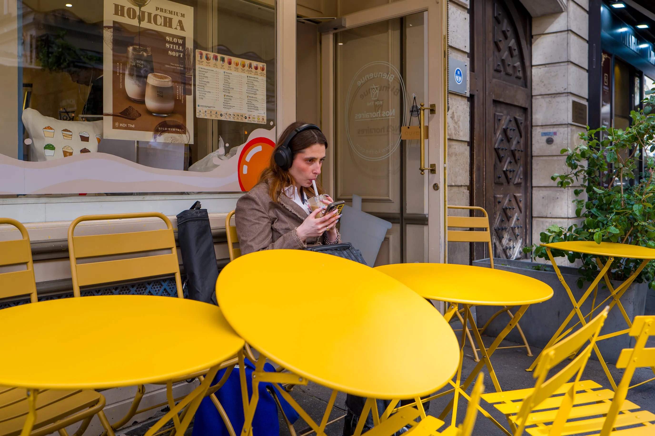 Une jeune femme déguste un bubble tea à une terrasse, près d'une table renversée.