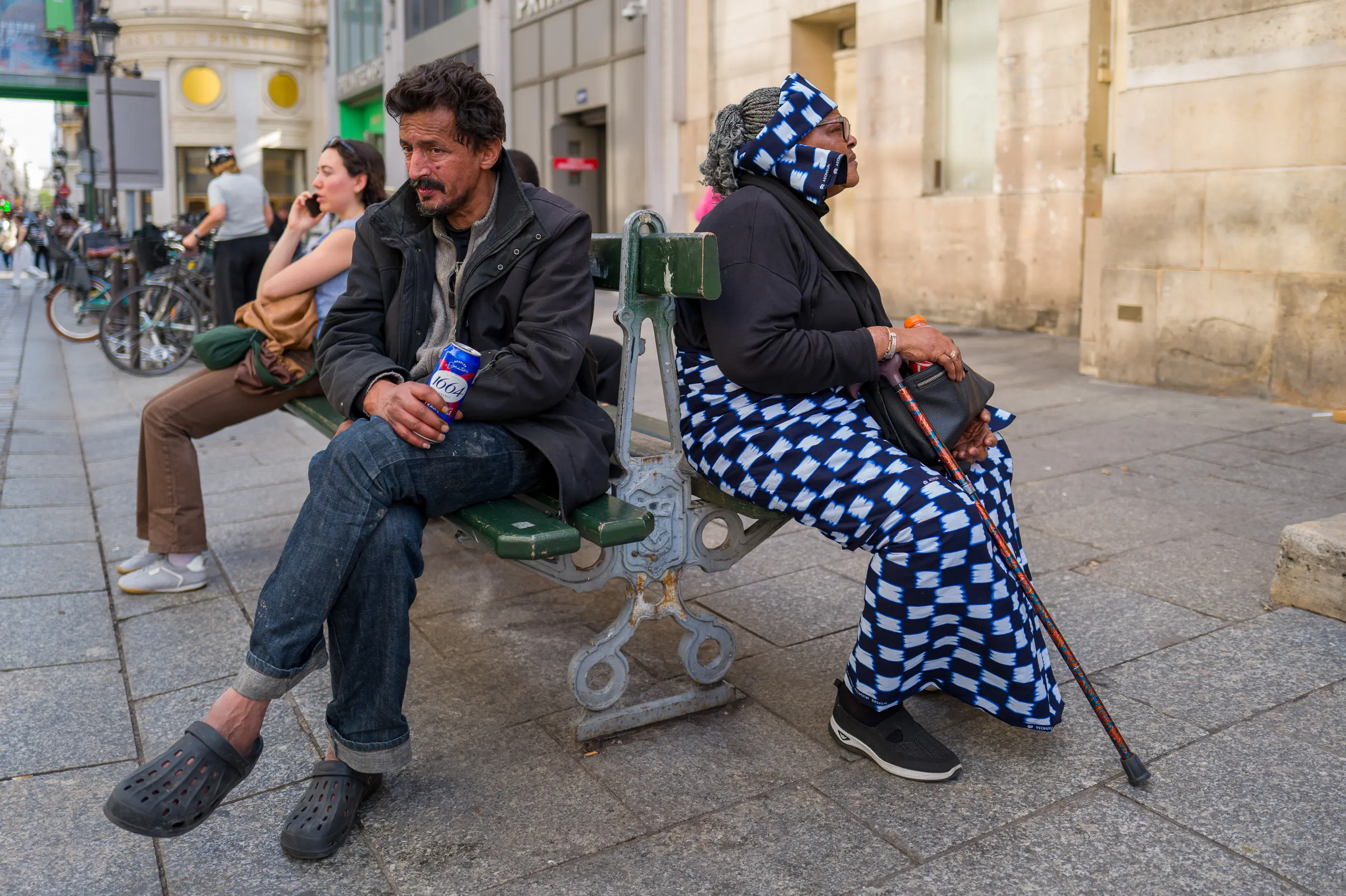 Rue de Caumartin, un homme buvant une bière et une femme attendant l'heure de la messe sont assis dos à dos sur le même banc