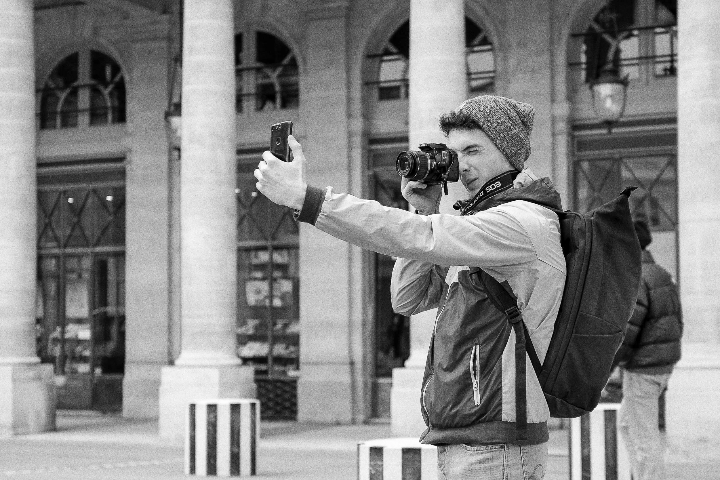 Un photographe regarde dans le viseur de son appareil tout en tenant un téléphone à bout de bras