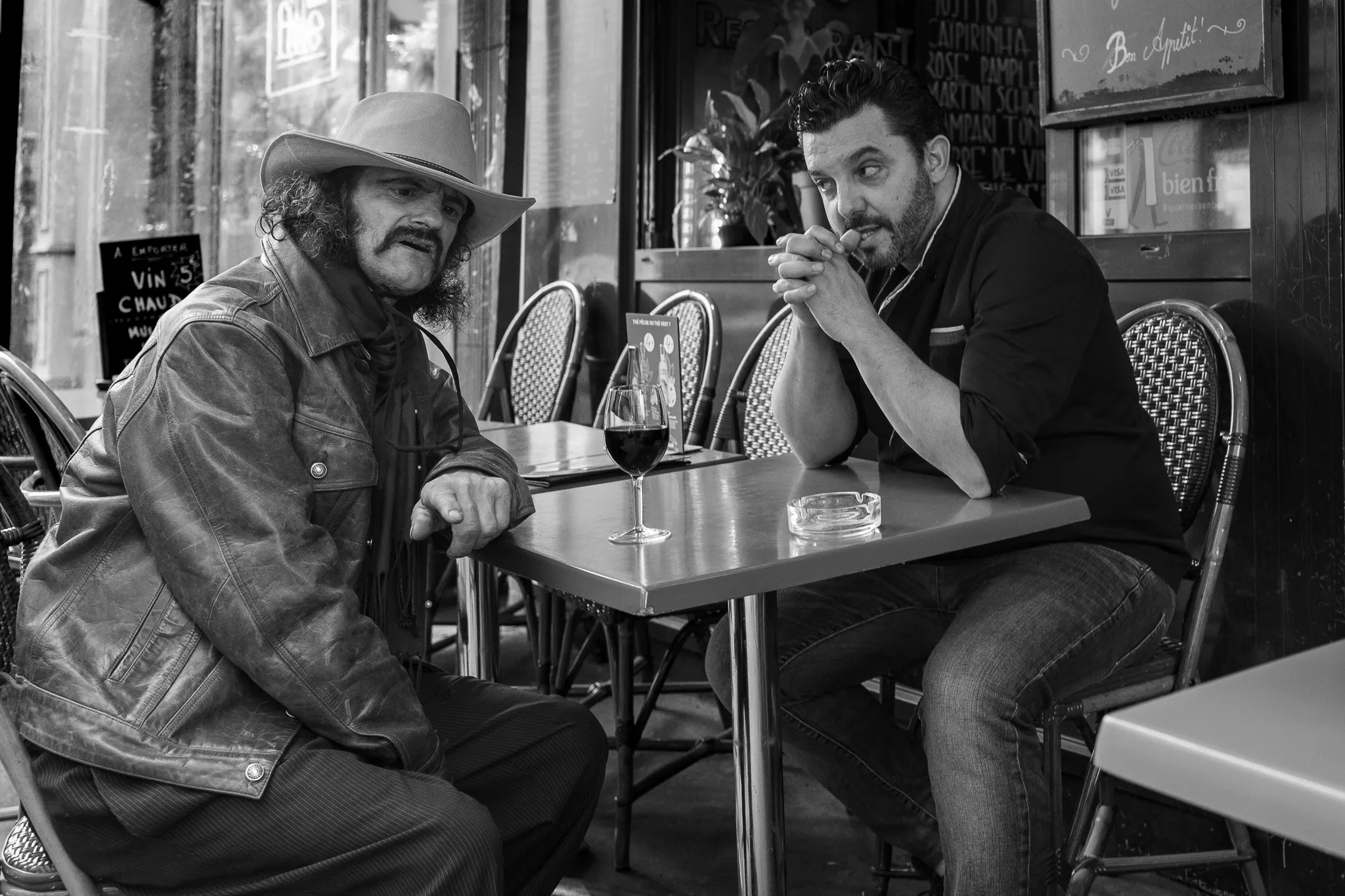 Deux hommes attablés à la terrasse d'un café parisien partagent un verre de vin et une conversation pleine de souvenirs.