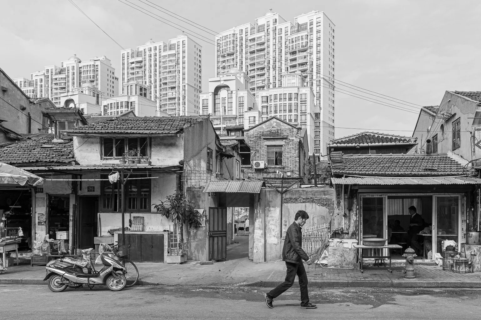 Dans un quartier de Shanghai en pleine métamorphose, le temps semble se figer et s'accélérer à la fois. La rue est un mélange de vieilles bâtisses, défigurées par l’usure et les années, et d’immeubles futuristes qui s’élèvent au-dessus, comme si la ville était prise dans une lutte entre son histoire et son avenir. 