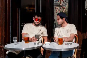 Deux hommes assis en terrasse devant une bière, l’un regardant son téléphone