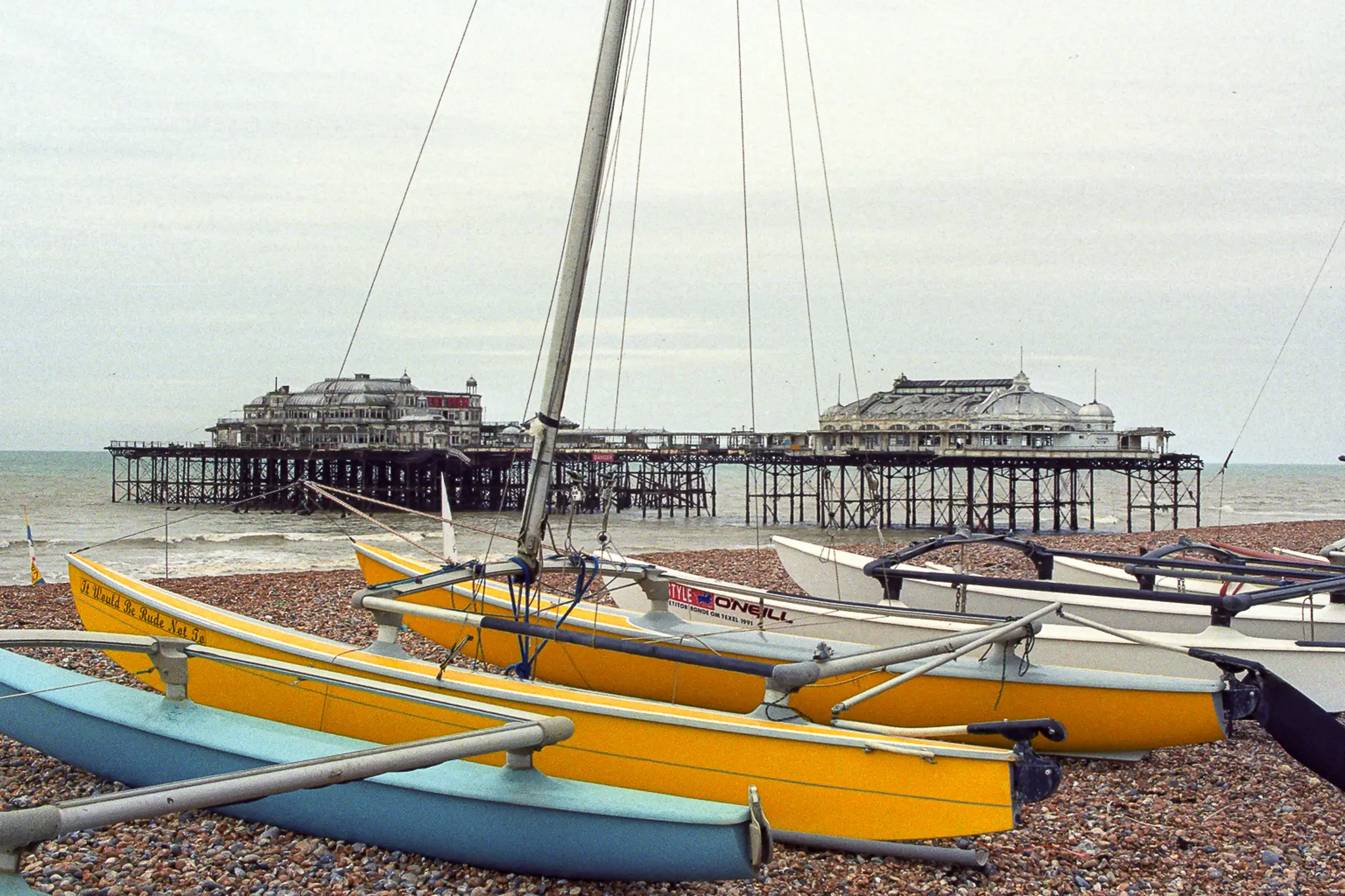 À Brighton au printemps 1994, des bateaux jaunes, bleus et orange occupent la plage de galets devant la silhouette sombre du West Pier fermé