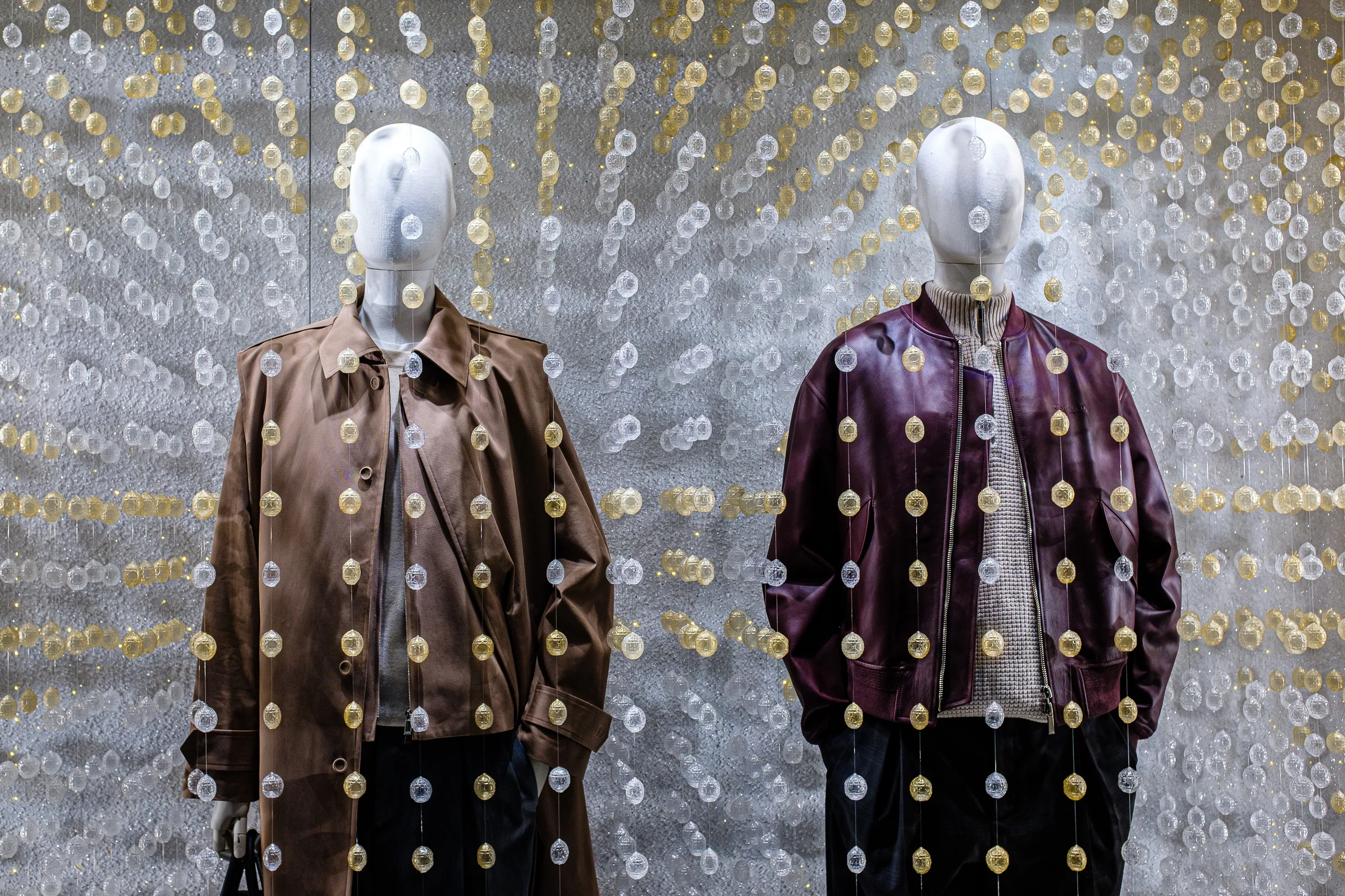 Deux mannequins sans visage en vitrine, vêtus de vestes en cuir sous une décoration de disques dorés.