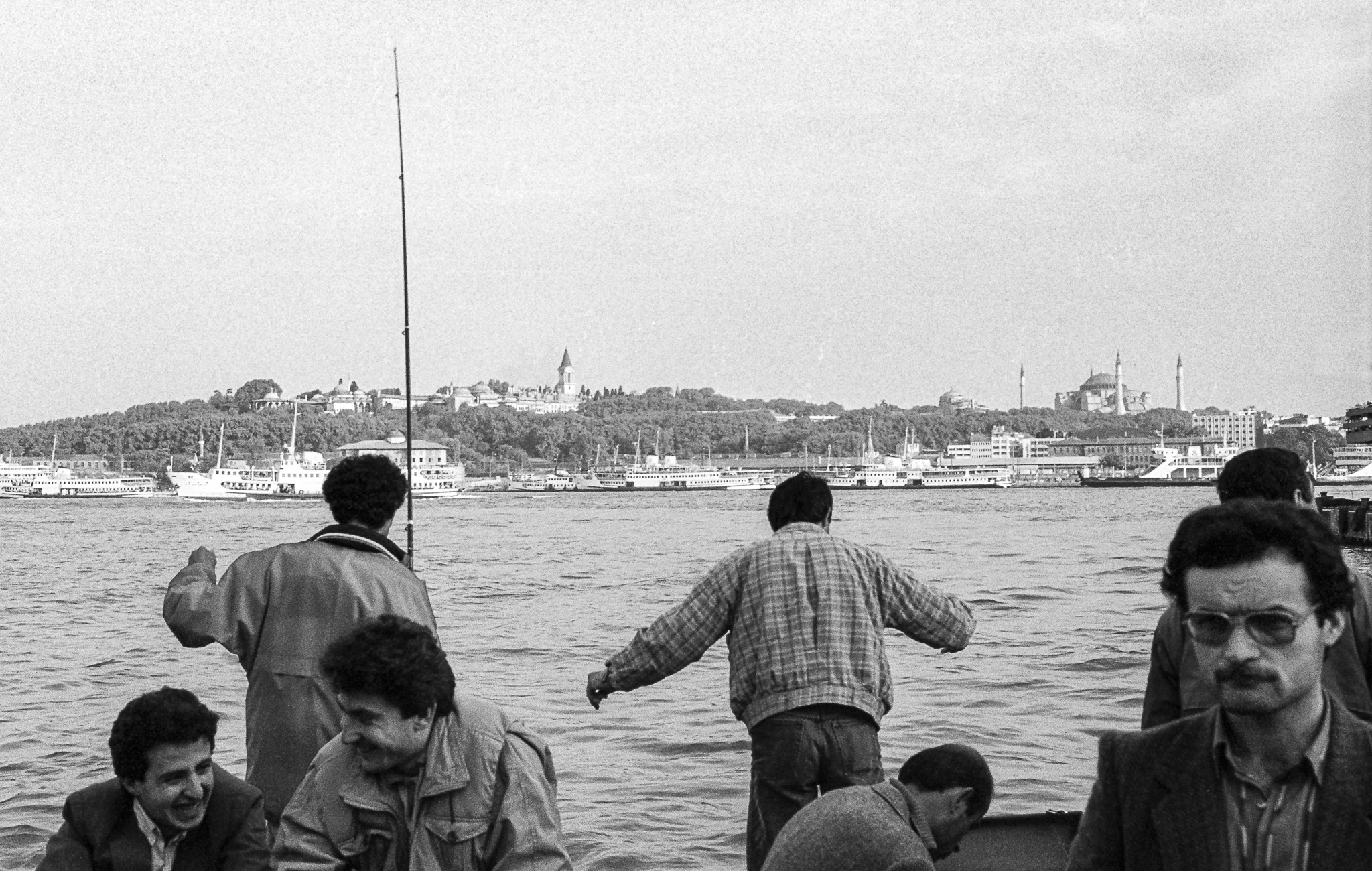 Des hommes pêchent depuis le quai d’Istanbul, avec la rive asiatique en arrière-plan.