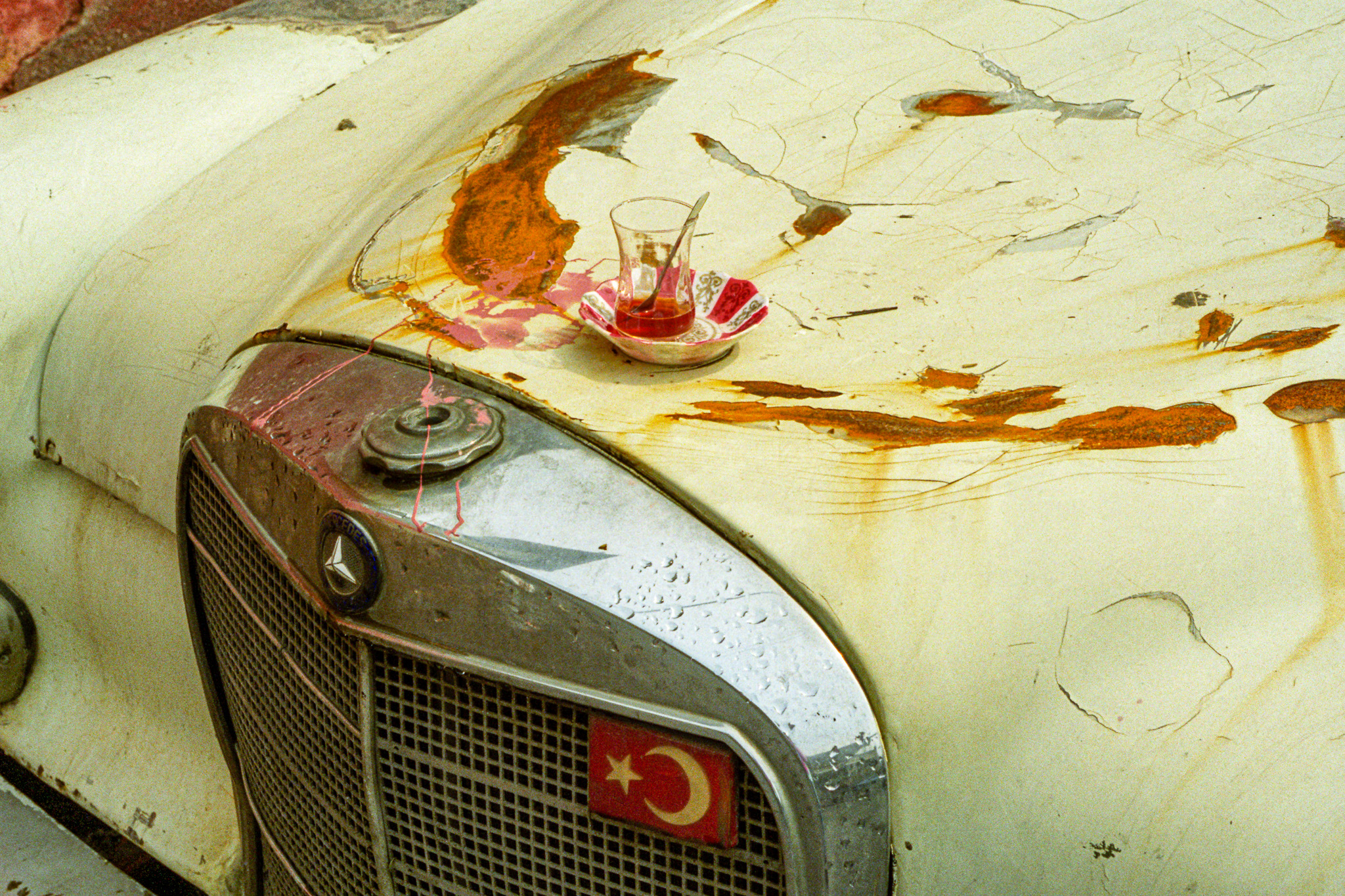 Un verre de thé turc posé sur une soucoupe à fleurs, installé sur le capot usé et rouillé d’une vieille Mercedes à Istanbul