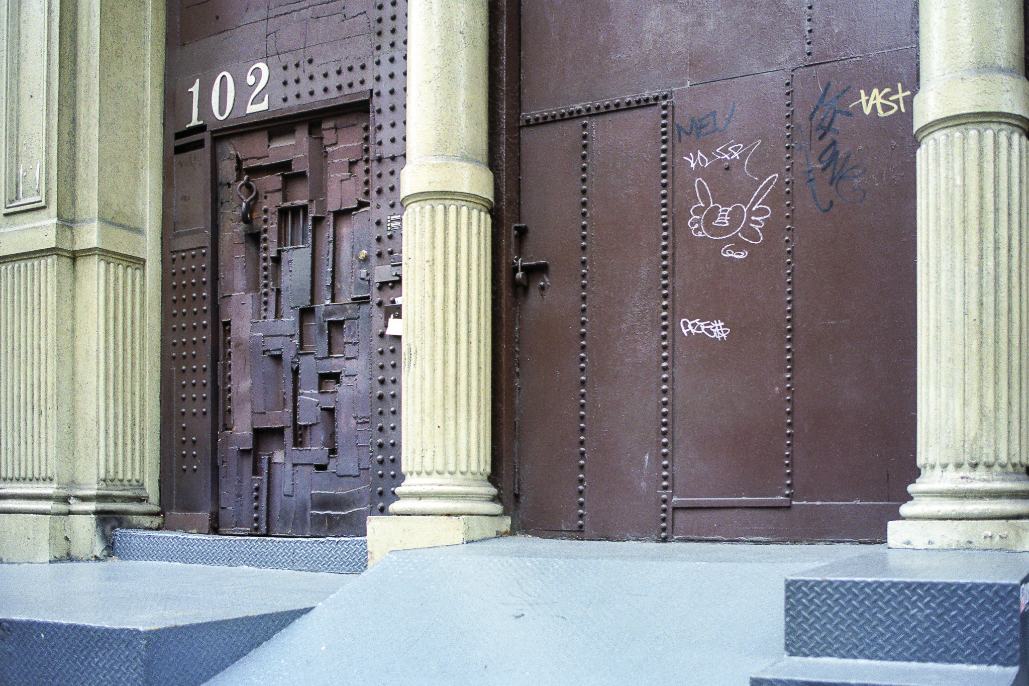 Porte métallique sculptée au 102 dans SoHo, New York 1995, encadrée de colonnes, entrée d’une galerie d’art.