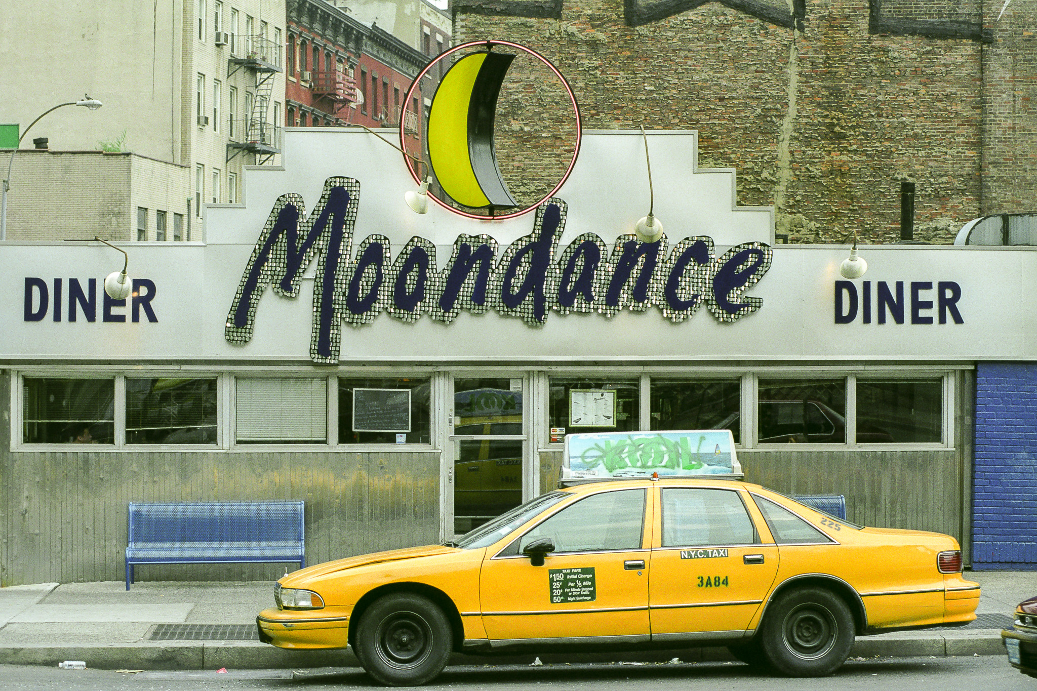 Moondance Diner à New York en 1995, façade argentée avec enseigne en forme de lune, taxi jaune garé devant.
