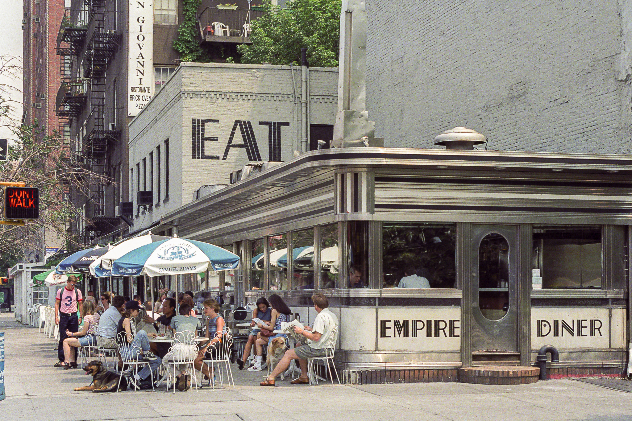 Empire Diner à New York en 1995, terrasse bondée sous des parasols, inscription EAT sur le mur.