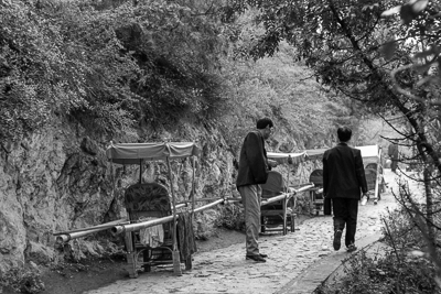 Deux porteurs font une pause près des chaises alignées au bord du sentier.
