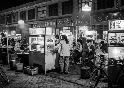 Clients attablés entre des vitrines de cuisine de rue et des bicyclettes à Xi’an en 1995