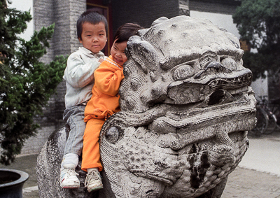 Deux enfants prennent place sur un lion de pierre dans l’enceinte du temple Da Ci’en.