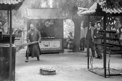 Un moine traverse la cour du temple, entre pavillons et présentoirs.