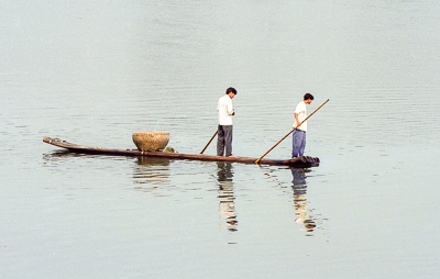 Deux pêcheurs sur une longue embarcation, dans le calme brumeux de Guilin.