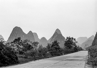 Route déserte avançant entre la végétation et les reliefs karstiques.