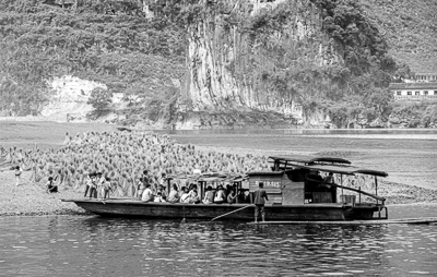Un bateau transportant des passagers longe une rive couverte de gerbes dressées.