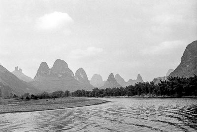 Une longue chaîne de pitons karstiques se découpe dans la brume au-dessus de la rivière.