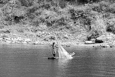 Un pêcheur debout sur un radeau relève son grand filet dans la rivière Li.