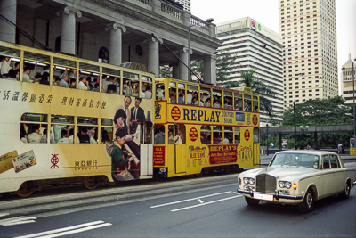 Un tramway à impériale et une automobile circulent entre les tours de l’île de Hong Kong.