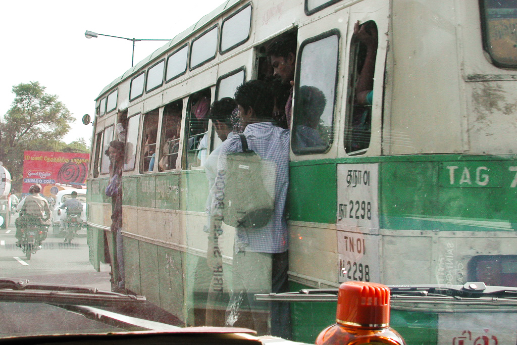 Un bus bondé, la porte ouverte, dépasse notre voiture.
