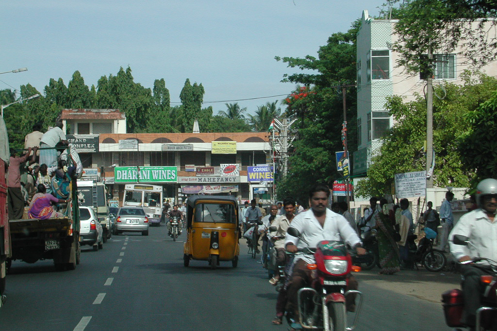 Un rickshaw et des motos dans une rue très animée.