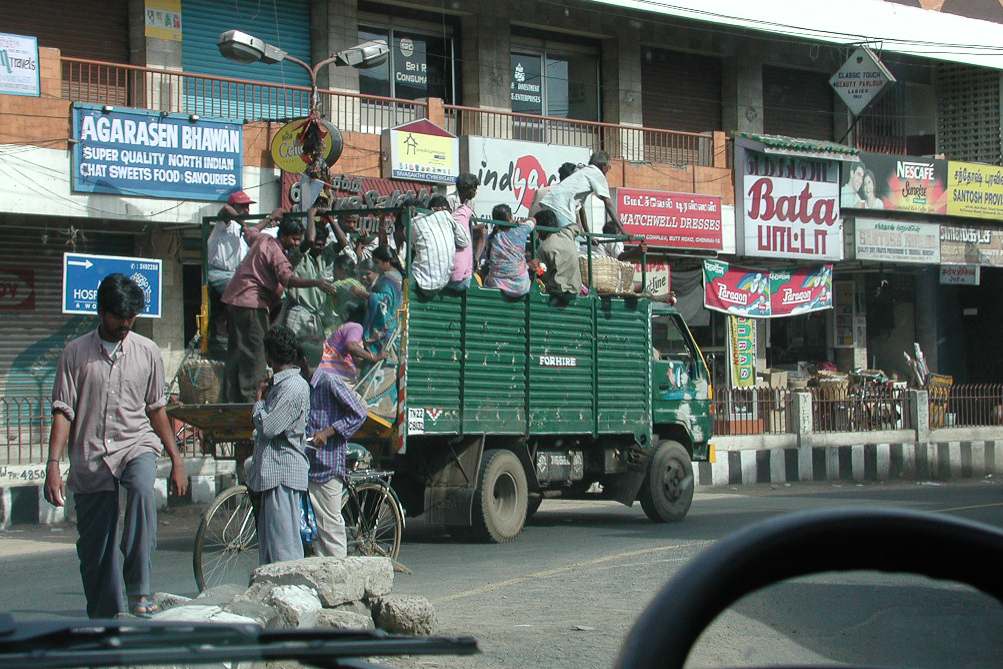 Passagers debout à l'arrière d'un petit camion vert.