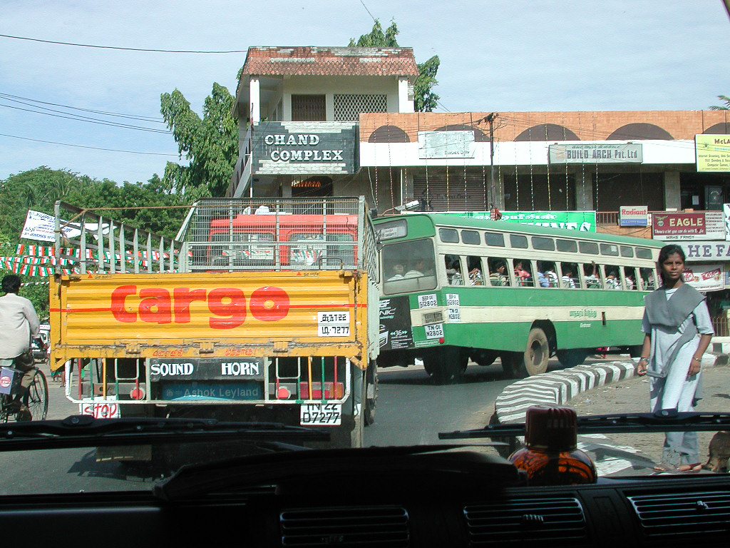 Camionnette, bus et piétons se croisent devant le Grand Complex.