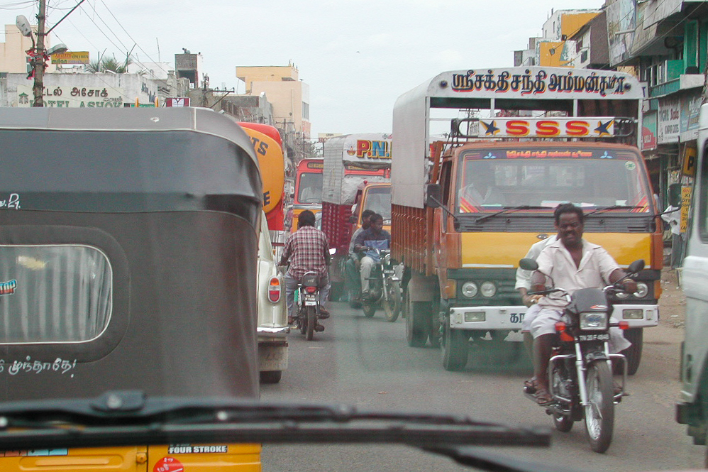 Rickshaw, camion et moto avancent de front.