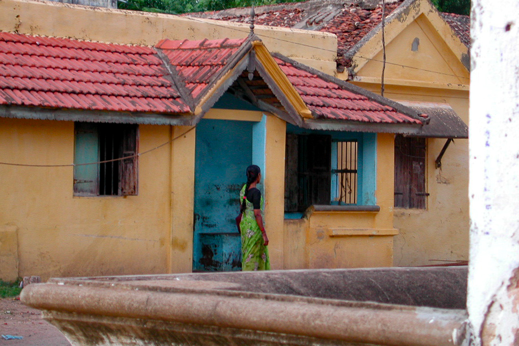 Une femme dans l'entrée bleue d'une petite maison jaune.