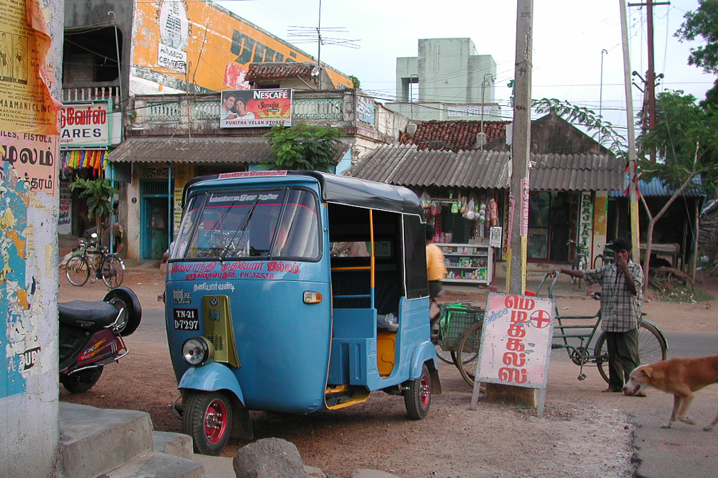 Un rickshaw bleu attend devant les commerces.