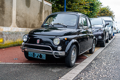 Petite Fiat 500 noire garée parmi les voitures anciennes à Épône