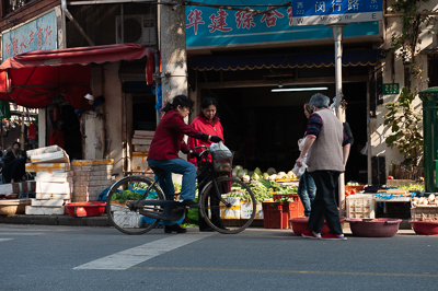 Vendeurs et clientes devant un commerce de fruits et légumes à Shanghai