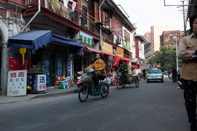 Petite rue commerçante parcourue par vélos et triporteurs à Shanghai