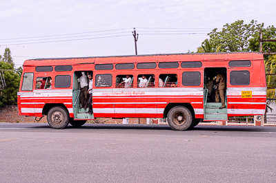 Un bus rouge roule portes ouvertes, les passagers visibles aux fenêtres.