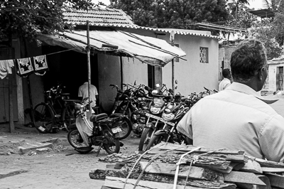 Un motocycliste chargé de planches passe devant un atelier rempli de deux-roues.