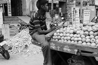 Un jeune vendeur est assis sur une charrette chargée de fruits.