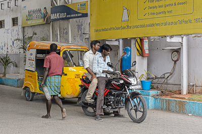 Un rickshaw et une moto se croisent devant un atelier de mécanique.