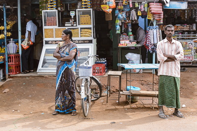 Une femme en sari et un homme en dhoti attendent devant une petite échoppe.