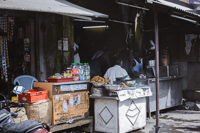 À l'ombre d'un auvent, une cantine de bord de route expose boissons, fruits et friandises.