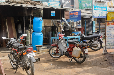 Bidons, outils et marchandises s'accumulent devant une échoppe desservie par les motocyclistes.