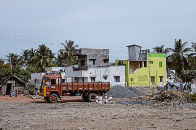 Un camion orange stationne sur un terrain de gravier devant des maisons vivement colorées.