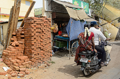 Une moto se glisse entre une pile de briques et une petite boutique couverte de bâches.