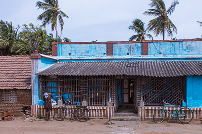 Des enfants observent la route derrière la grille d'une longue maison peinte en bleu.